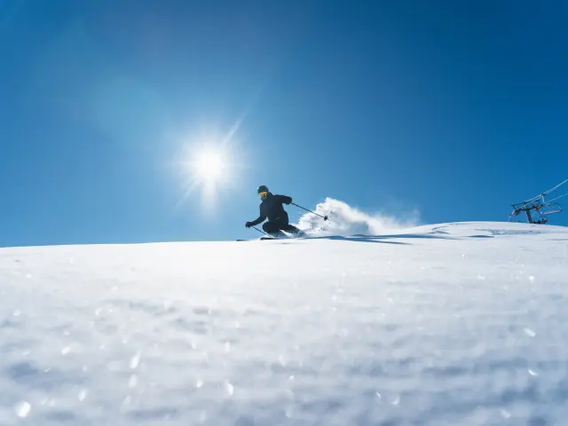 Skieur descendant une piste enneigée sous un grand soleil sur le domaine alpin du Dévoluy.