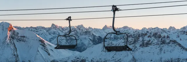 Deux télésièges vides au-dessus des montagnes enneigées du Dévoluy au lever du soleil.