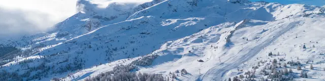 Vue aérienne du domaine skiable du Dévoluy enneigé, entre forêts et pistes de ski.