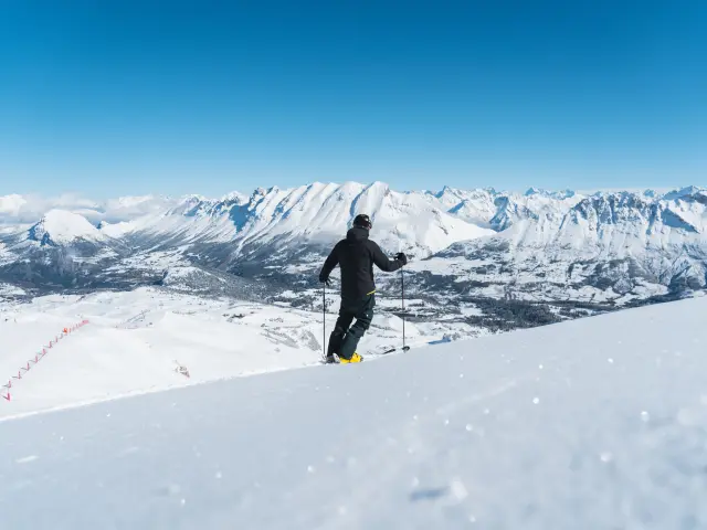 Skieur observant le paysage enneigé du massif du Dévoluy depuis une piste du domaine skiable.